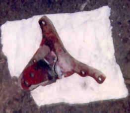 1989 Ford Bronco - A close-up view of a rusted metal bracket, possibly a vehicle part, with visible red paint flecks and the Supermotors logo at the bottom.