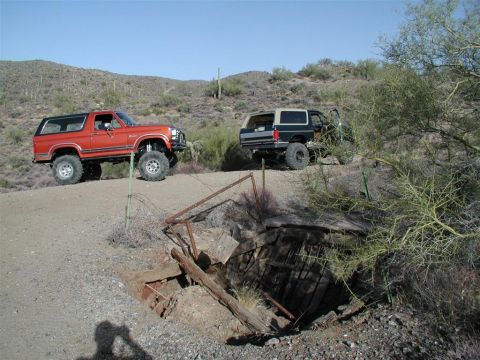 1994 Ford Bronco - Two Ford Broncos navigate a desert terrain with a mine shaft in the foreground.