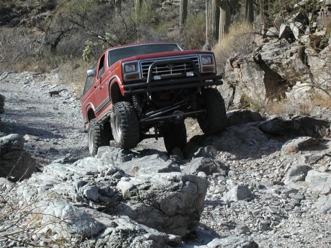 1994 Ford Bronco - This red SUV is shown traversing a difficult, rocky terrain with large boulders.