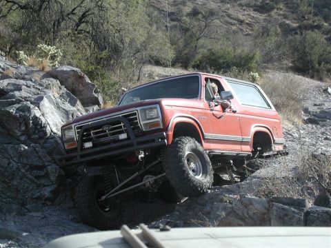 1994 Ford Bronco - This red Ford Bronco is shown off-roading on a steep, rocky incline.