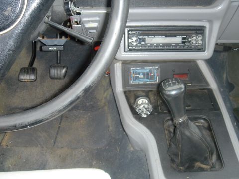 1986 Ford Mustang - Close-up of the driver's side interior, pedals, a manual gear shifter, and an aftermarket radio.