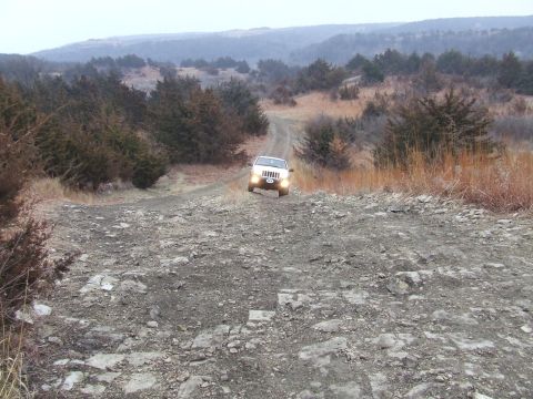 1994 Ford Bronco - A white SUV navigates a challenging, rocky terrain on an off-road trail surrounded by dry brush and trees.