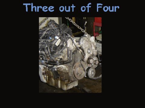 1991 Ford LTD Crown Victoria - A bare aluminum V-type engine hangs from a hoist chain in a garage, shown from the accessory-drive end with the crank pulley, timing cover…
