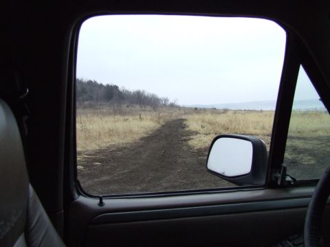 1994 Ford Bronco - The view from the passenger seat shows a dirt road leading through a dry, grassy field under an overcast sky.