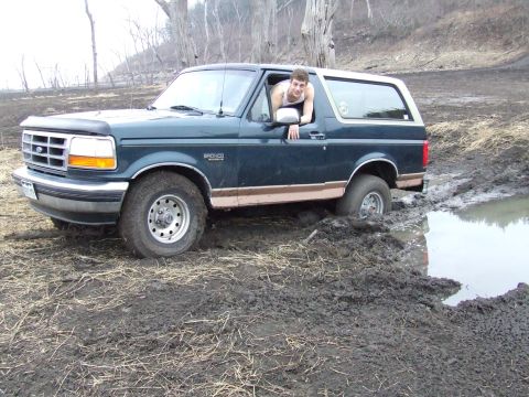 1994 Ford Bronco - A man looks out the window of a dark green Ford Bronco that is stuck in a muddy area.