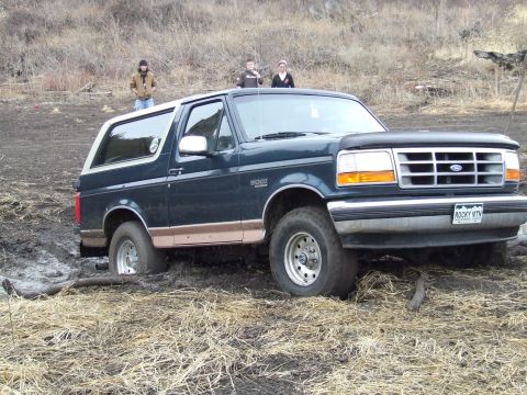 1994 Ford Bronco - A 1994 Ford Bronco is stuck in a muddy area with dry grass and hills in the background.