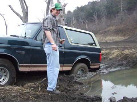 1994 Ford Bronco - A dark green 1994 Ford Bronco is stuck in the mud with a man standing beside it.
