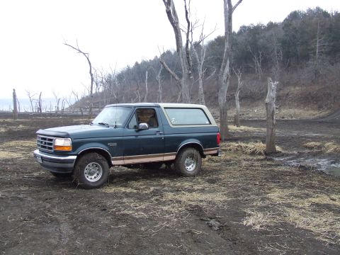 1994 Ford Bronco - This 1994 Ford Bronco is parked in a desolate, muddy area with bare trees and a body of water in the background.