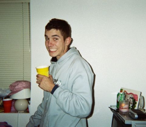 1994 Mazda MX-3 - A man smiles while holding a yellow cup. The background shows a wall and some items on a shelf.