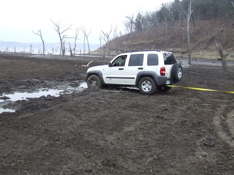 1994 Ford Bronco - A white SUV is stuck in a muddy field with bare trees and a body of water in the background.