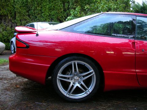 1996 Ford Probe - A red coupe with a spoiler and aftermarket wheels is parked outside on a wet day.
