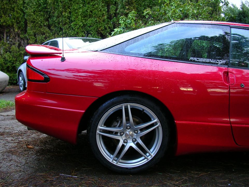 Red coupe with a spoiler and aftermarket wheels, seen from the rear quarter