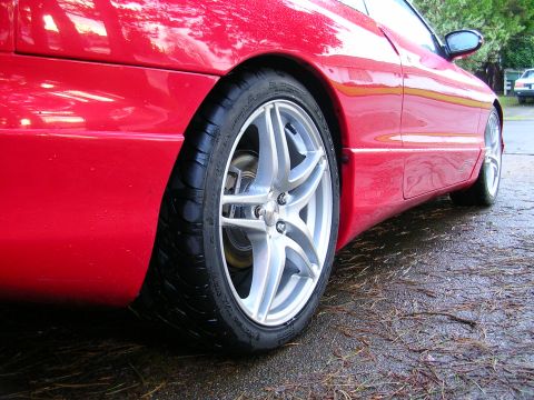 1996 Ford Probe - A red 1996 Ford Probe is viewed from the side, focusing on its rear wheel and lower body panel.