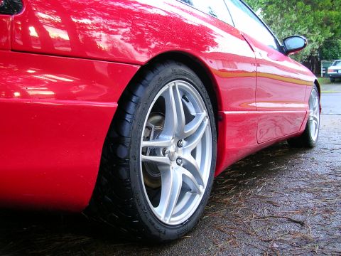 1996 Ford Probe - A red car with custom wheels is parked on a wet surface, reflecting the surrounding trees.