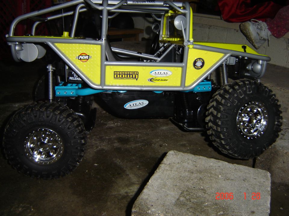 Yellow remote control rock crawler toy with silver roll cage and large off-road tires, side view