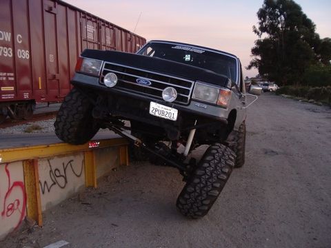 1989 Ford Bronco - This heavily modified Ford truck is positioned precariously on a ledge, with a train car nearby.