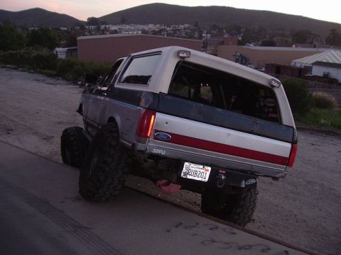 1989 Ford Bronco - Modified Ford Bronco with large off-road tires is seen from behind on a dirt road.