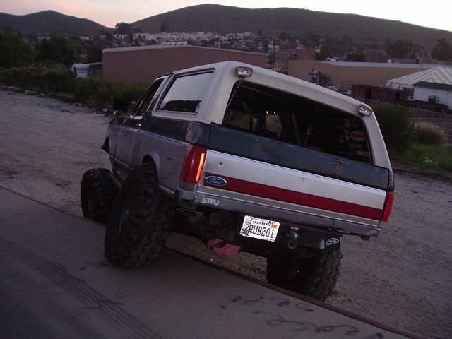 Lifted white and gray Ford Bronco SUV on big off-road tires, rear view at dusk