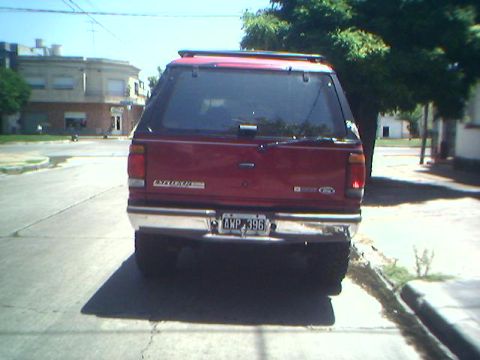 1996 Ford Explorer - Rear view of a red Ford Explorer SUV parked on a street with a tree and buildings in the background.
