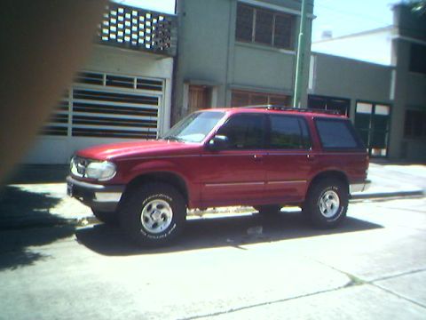 1996 Ford Explorer - Side view of a red 1996 Ford Explorer SUV parked in front of a building.