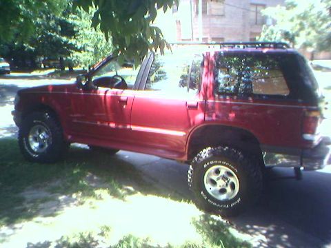 1996 Ford Explorer - This red SUV is parked on a residential street, showing its side profile with a roof rack and tires.