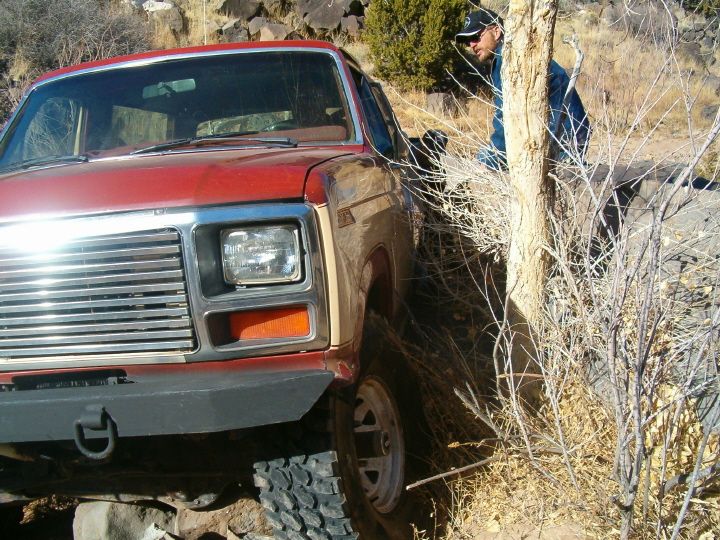 Red full-size Dodge 4x4 truck nosed down into a rocky ditch off-road, man watching nearby
