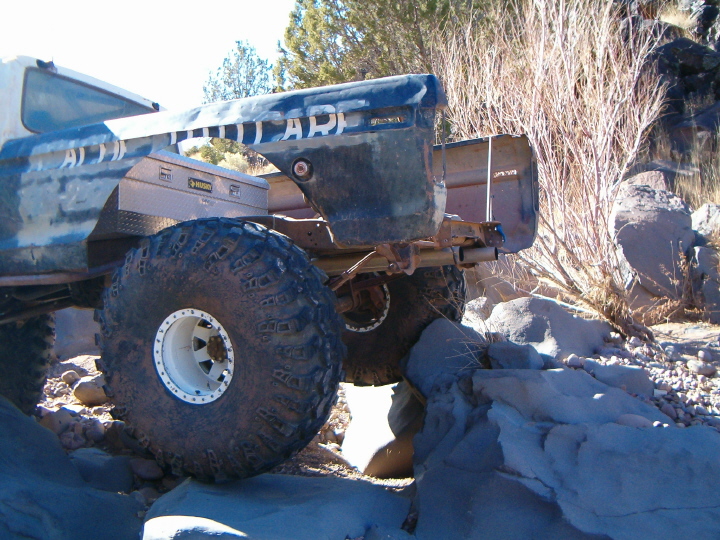 Rear of muddy blue 4x4 with huge mud tires and beadlock wheels parked among boulders