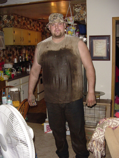 1989 Ford Bronco - A man stands indoors, his shirt heavily stained with mud, wearing a camouflage bucket hat.