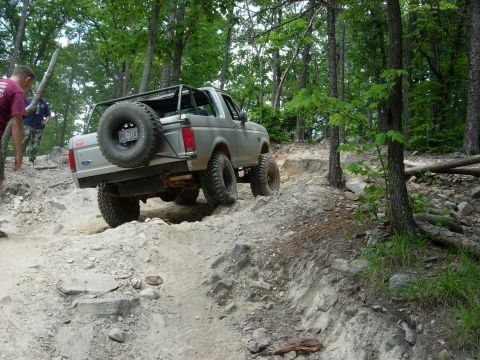 1995 Ford Bronco - A 1995 Ford Bronco navigates a challenging rocky off-road trail surrounded by trees.