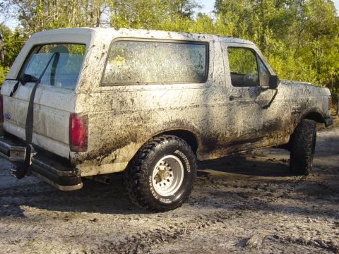 1989 Ford Bronco - This heavily mud-covered Ford Bronco is seen from a three-quarter front angle, revealing its distinctive body style.