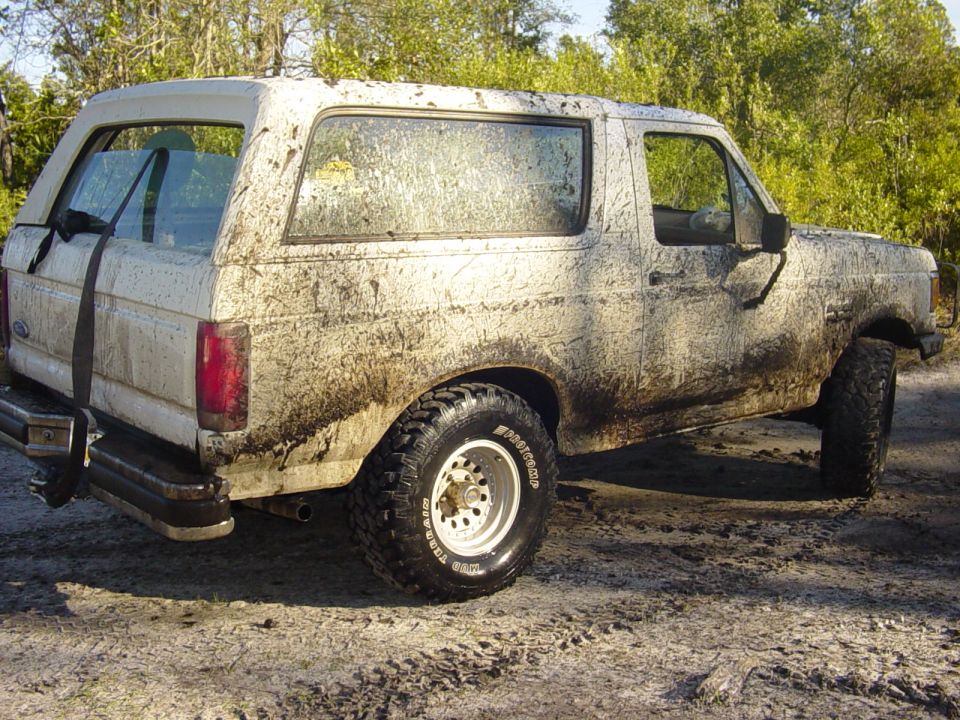 Mud-splattered white Ford Bronco from the side, showing its rear quarter panel and side window