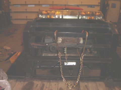 1992 Ford Bronco - Front view of a tow truck, equipped with chains and amber warning lights, parked indoors.