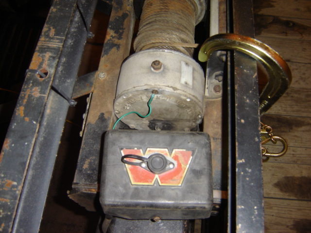 Winch motor and control box on a trailer frame. A C-clamp is holding a metal bar