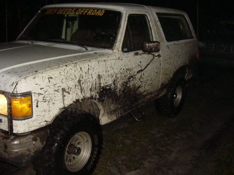 1989 Ford Bronco - This white 1989 Ford Bronco is heavily covered in mud, with a 'DIRTY DEEDS OFFROAD' decal visible on the windshield.