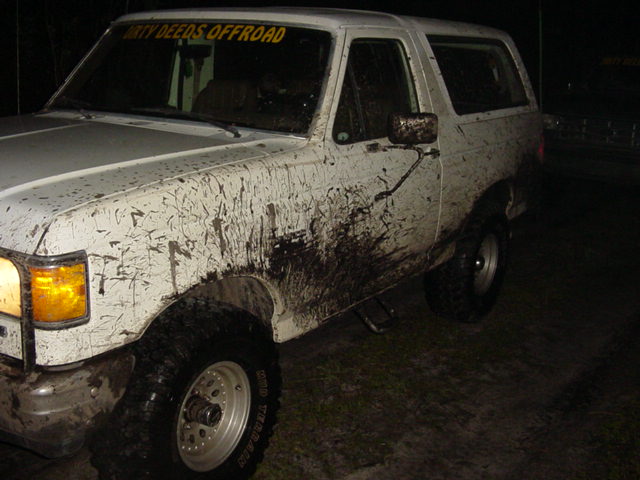 Mud-splattered white 1989 Ford Bronco, 3/4 front view. Yellow 'DIRTY DEEDS OFFROAD' decal on windshield