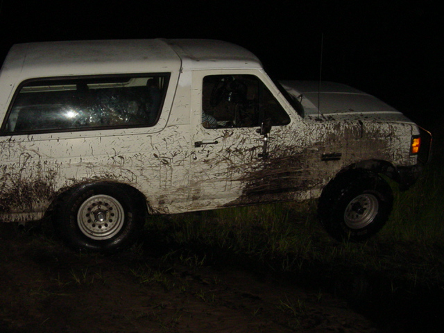 White SUV covered in mud, parked on uneven ground at night