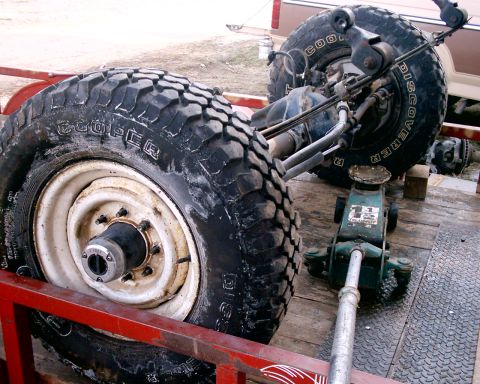 1985 Ford Bronco - The rear axle and tires of a vehicle are loaded onto a trailer, supported by a jack.