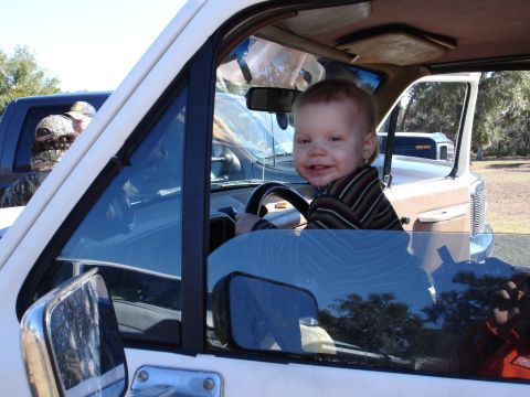 1989 Ford Bronco - A young child smiles while sitting in the driver's seat of a vehicle, with other vehicles in the background.