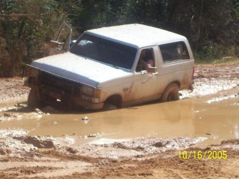 1989 Ford Bronco - A white 1989 Ford Bronco is stuck deep in mud, with the driver's door ajar.