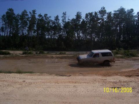 1989 Ford Bronco - White 1989 Ford Bronco navigating a muddy off-road course on a sunny day.