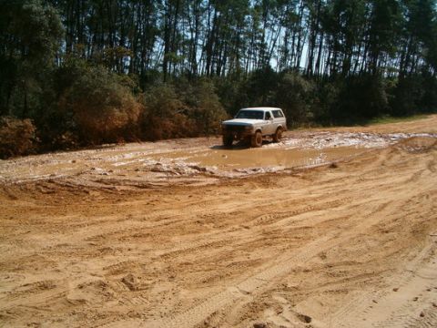 1989 Ford Bronco - A white 1987 Ford Bronco navigates a muddy trail, kicking up water and dirt.