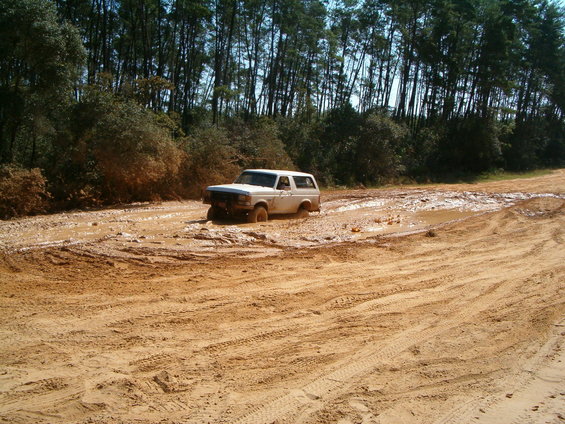 1989 Ford Bronco stuck in a muddy trail with trees in the background