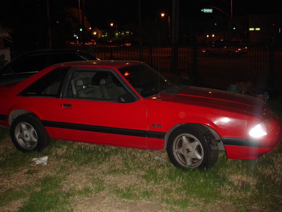 Red coupe with black side molding and 5.0 fender badge. Four-lug wheels are visible