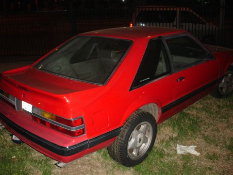 1993 Ford Taurus - A red coupe with a black trim and a spoiler is parked on grass.