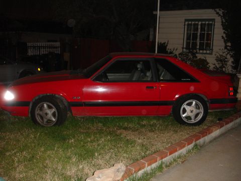 1993 Ford Taurus - Side view of a red coupe with black side trim and a 5.0 badge, likely a Ford Mustang.