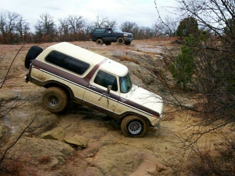 1993 Ford Bronco - Elevated side view of a cream and brown two-tone late-1970s Ford Bronco descending a steep sandstone slab, mud streaking its lower body. It…