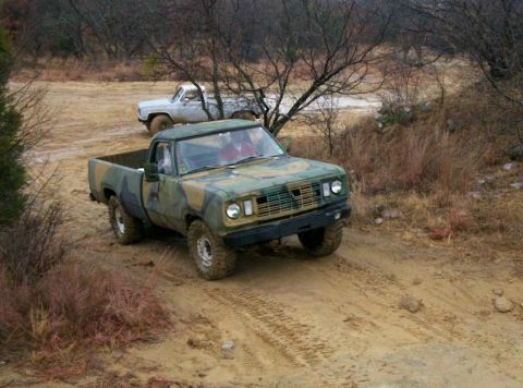 1993 Ford Bronco - A camouflage-painted 1970s Dodge regular-cab 4x4 pickup with no doors climbs a muddy dirt incline, riding on mud-terrain tires and white st…