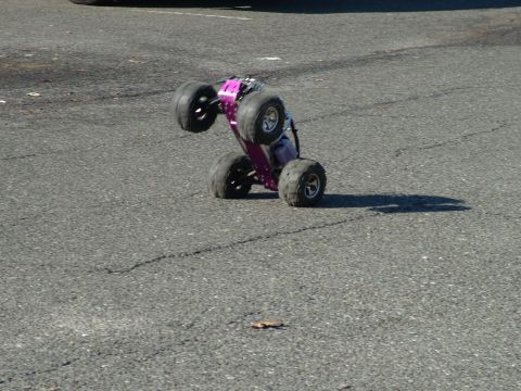 1994 Ford Bronco - A purple remote control monster truck is captured mid-air, balancing on its rear wheels on an asphalt surface.