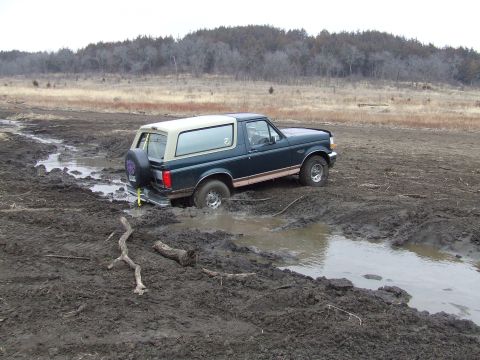 1994 Ford Bronco - A 1994 Ford Bronco navigates a muddy trail, with its rear wheel deep in the mire.
