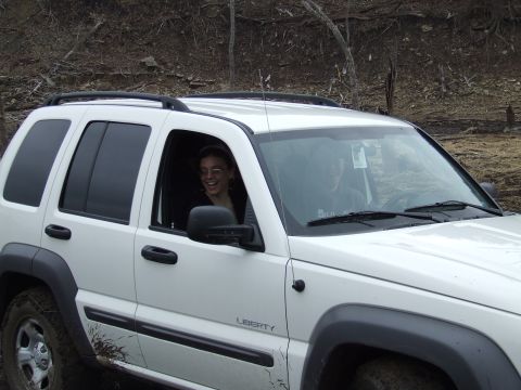 1994 Ford Bronco - White Jeep Liberty with two occupants driving off-road. Mud is visible on the vehicle's lower panels.